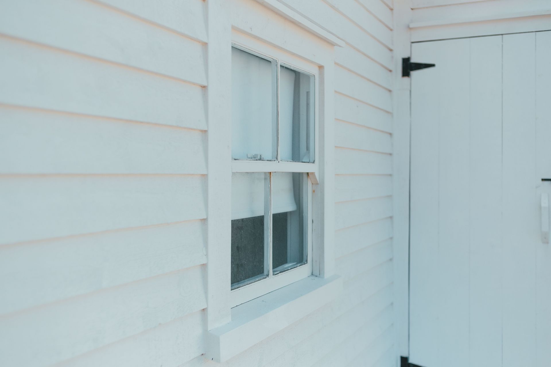 Close-up of a white wooden facade showcasing a window and door, highlighting minimalist architecture.